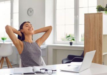 Smiling Woman Sitting in the Office in Front of a Laptop and Stretching after Work